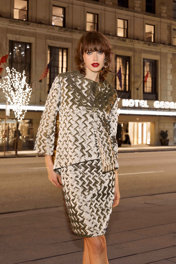 Woman in a patterned outfit standing in front of a hotel at night.