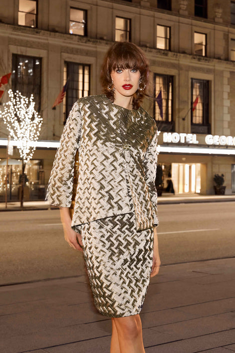 Woman in a patterned outfit standing in front of a hotel at night.