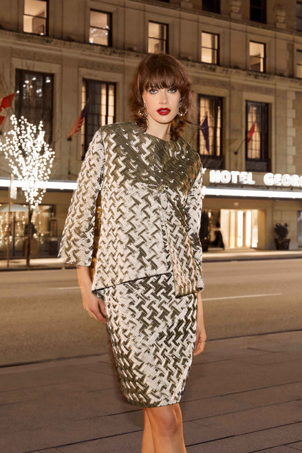 Woman in a patterned outfit standing in front of a hotel at night.