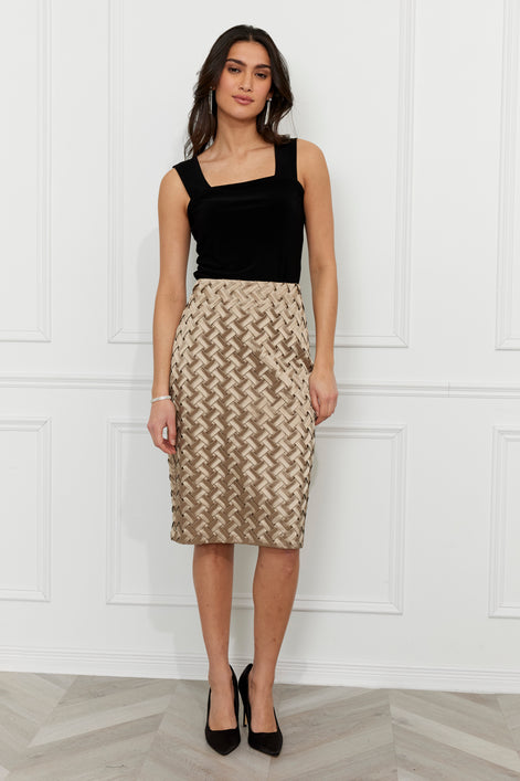 Woman wearing a black top and patterned skirt against a white paneled wall.