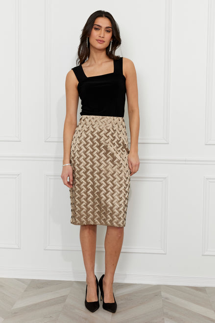 Woman wearing a black top and patterned skirt against a white paneled wall.