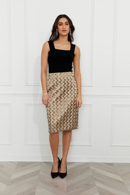 Woman wearing a black top and patterned skirt against a white paneled wall.