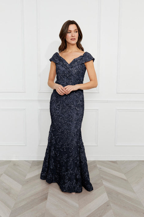 Woman wearing a navy blue evening gown against a white paneled wall.