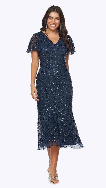 A woman wearing a navy blue sequined midi dress with short flutter sleeves and a V-neckline, mid-calf in length.