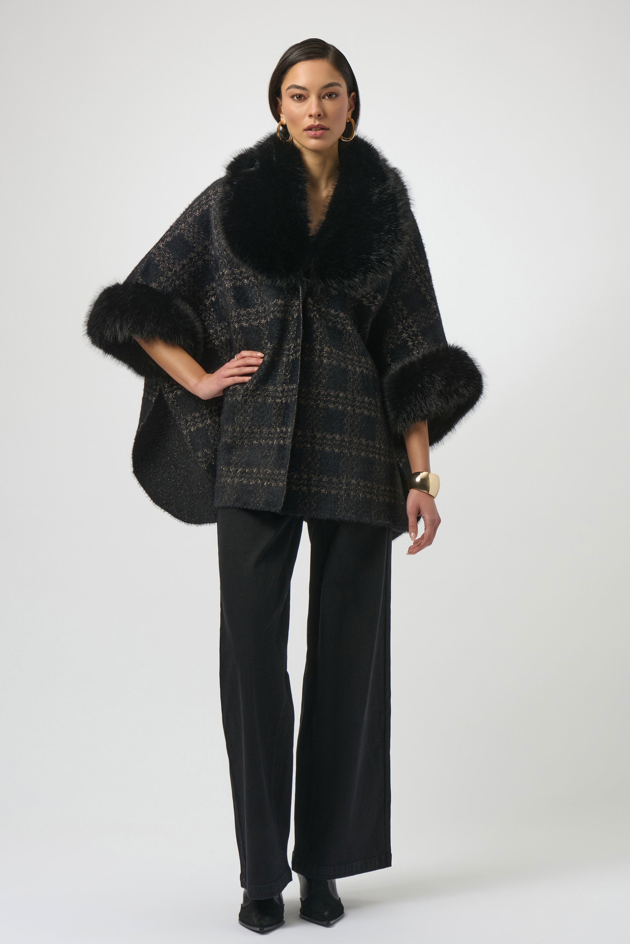 Woman wearing a black plaid poncho with fur trim on a white background