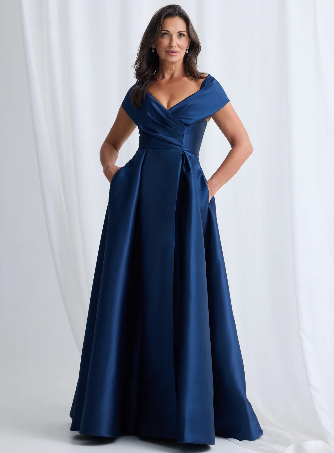 Woman wearing a blue evening gown against a white curtain background