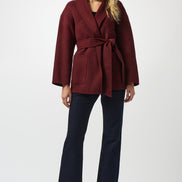 Woman wearing a burgundy coat and navy pants on a white background