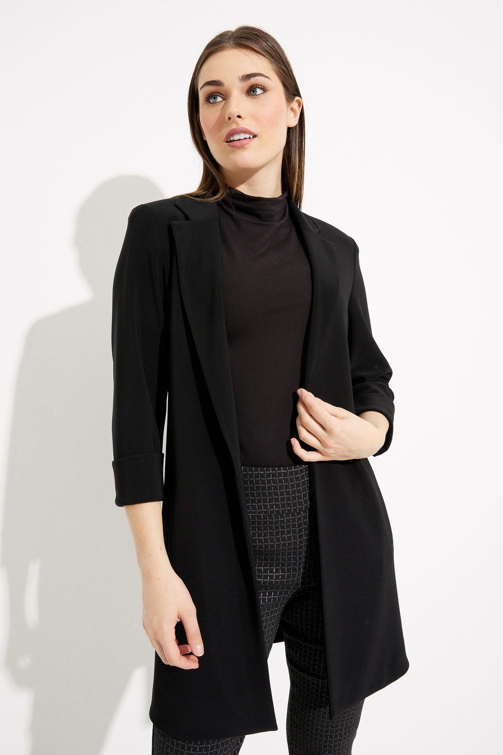 Woman wearing a black coat over a black top and plaid pants on a white background