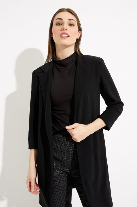 Woman wearing a black coat over a black turtleneck and patterned pants on a white background