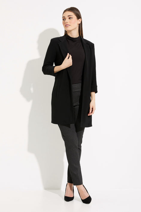 Woman wearing a black coat, black turtleneck, and gray pants on a white background