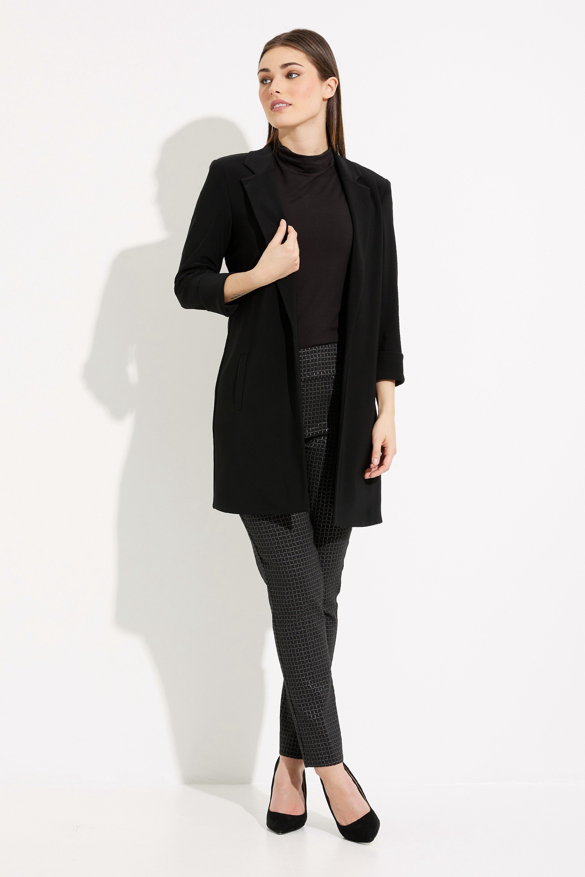 Woman wearing a black coat, black turtleneck, and gray pants on a white background