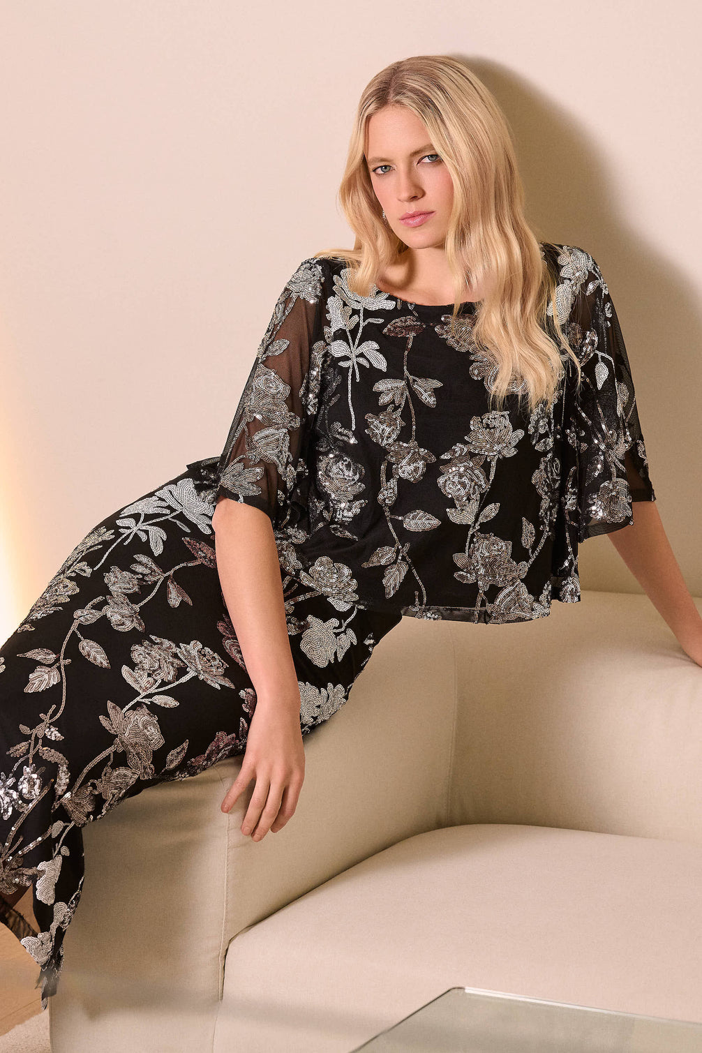 Woman wearing a black floral dress sitting on a beige couch.