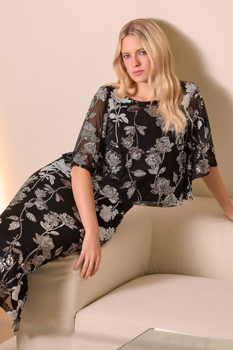 Woman wearing a black floral dress sitting on a beige couch.