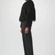 Woman wearing a black fringed jacket, black pants, and black boots on a white background