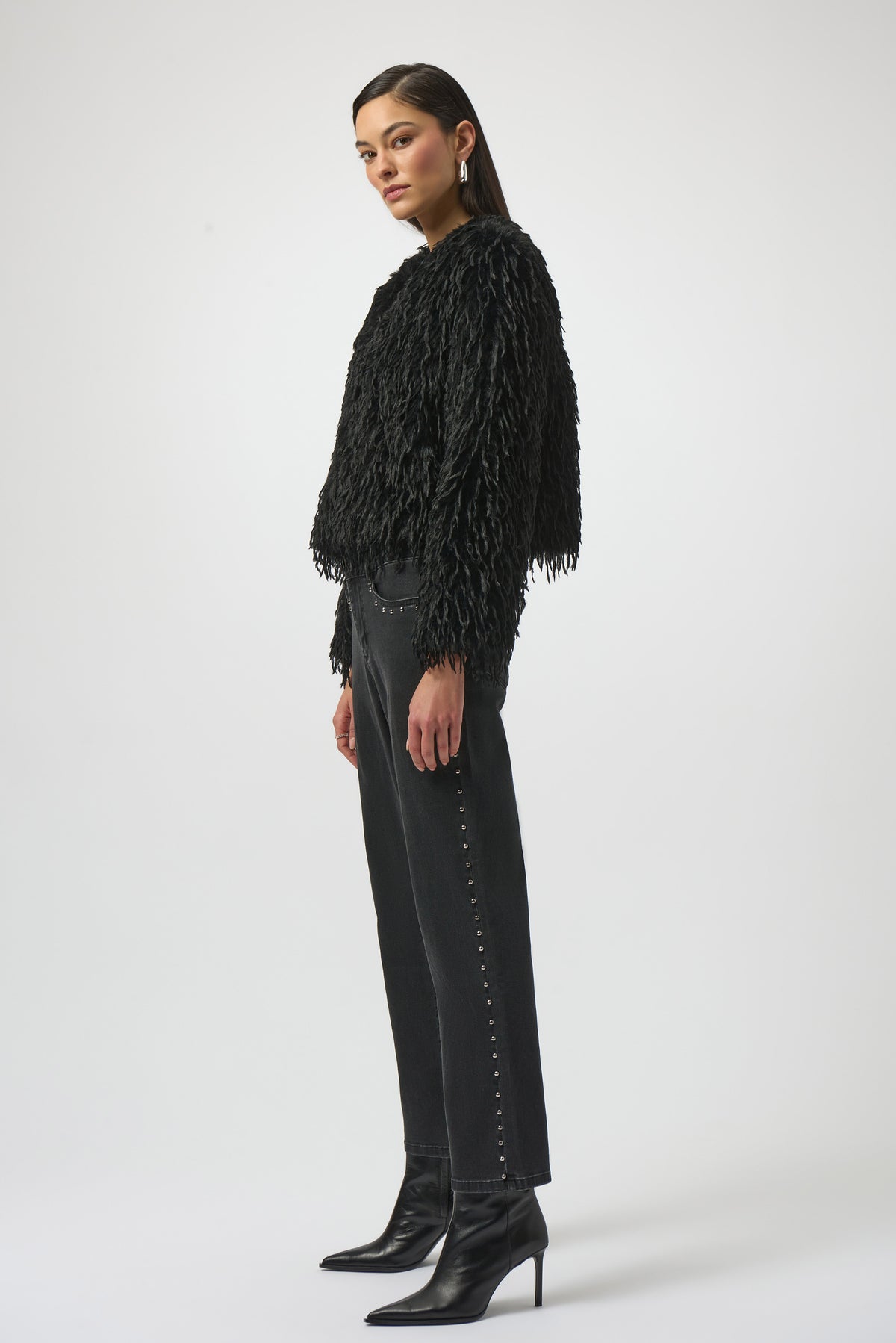 Woman wearing a black fringed jacket, black pants, and black boots on a white background