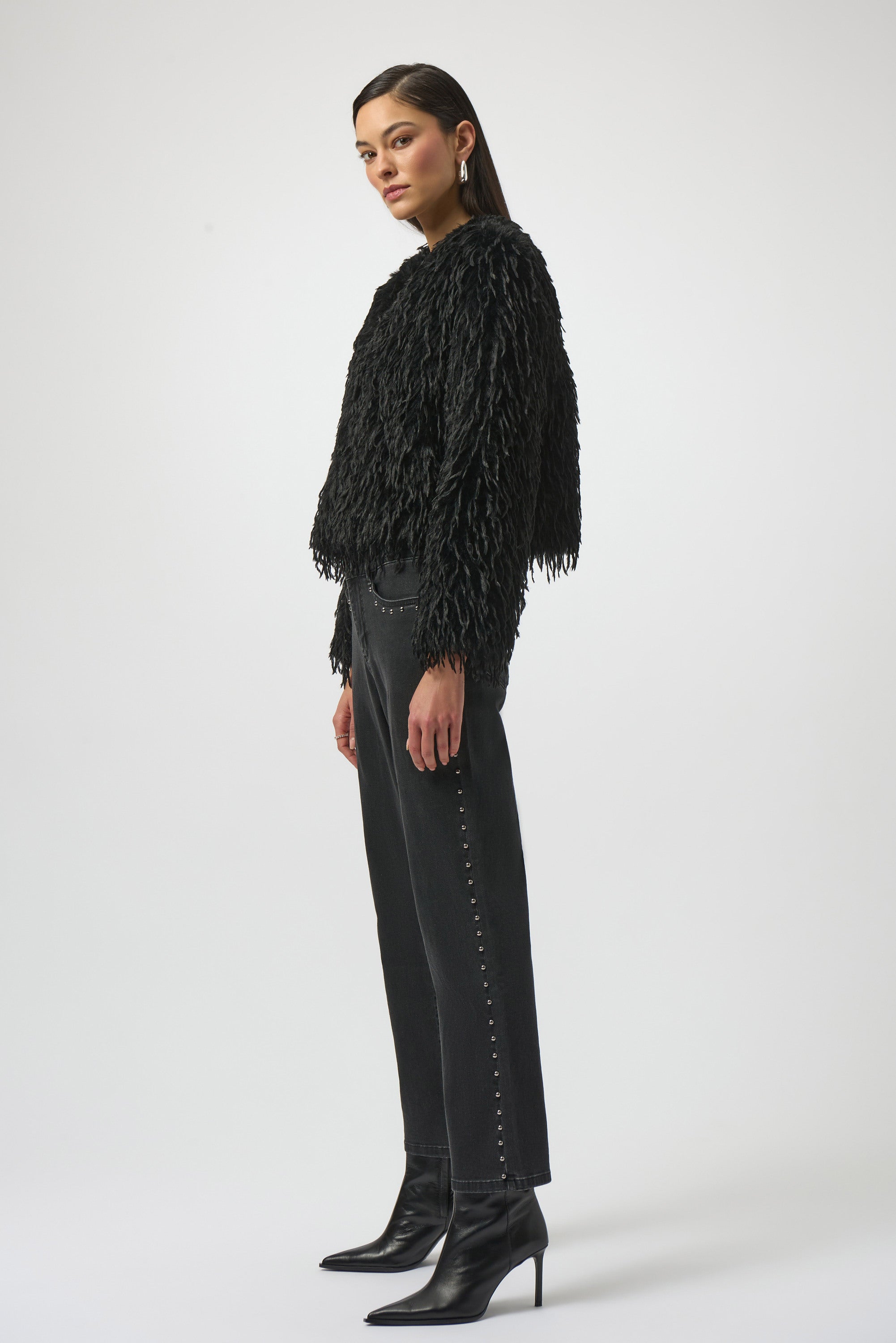 Woman wearing a black fringed jacket, black pants, and black boots on a white background