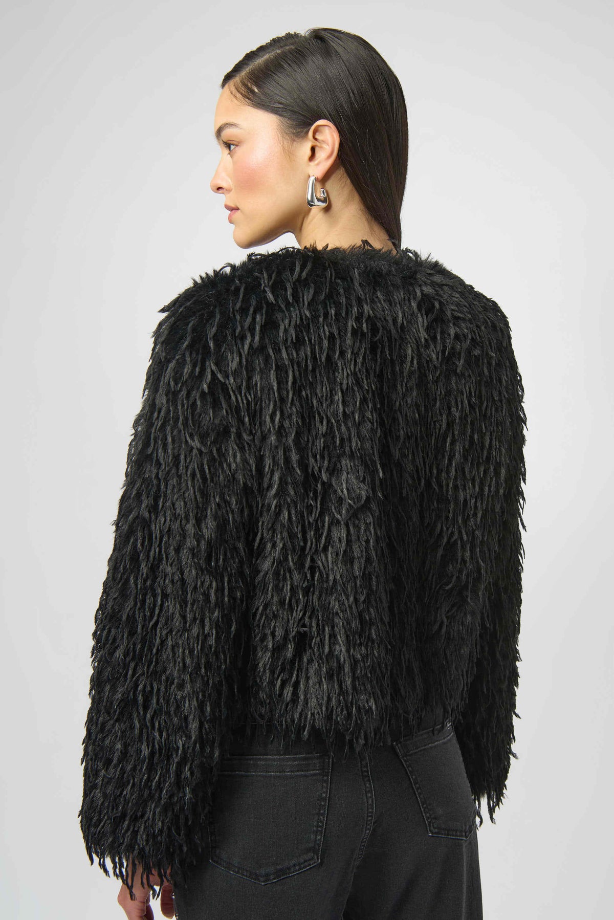 Person wearing a black fluffy jacket on a plain background