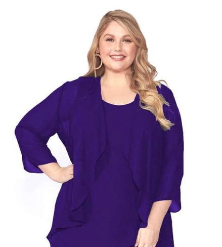 A woman standing and posing in an elegant purple chiffon dress and matching jacket set.